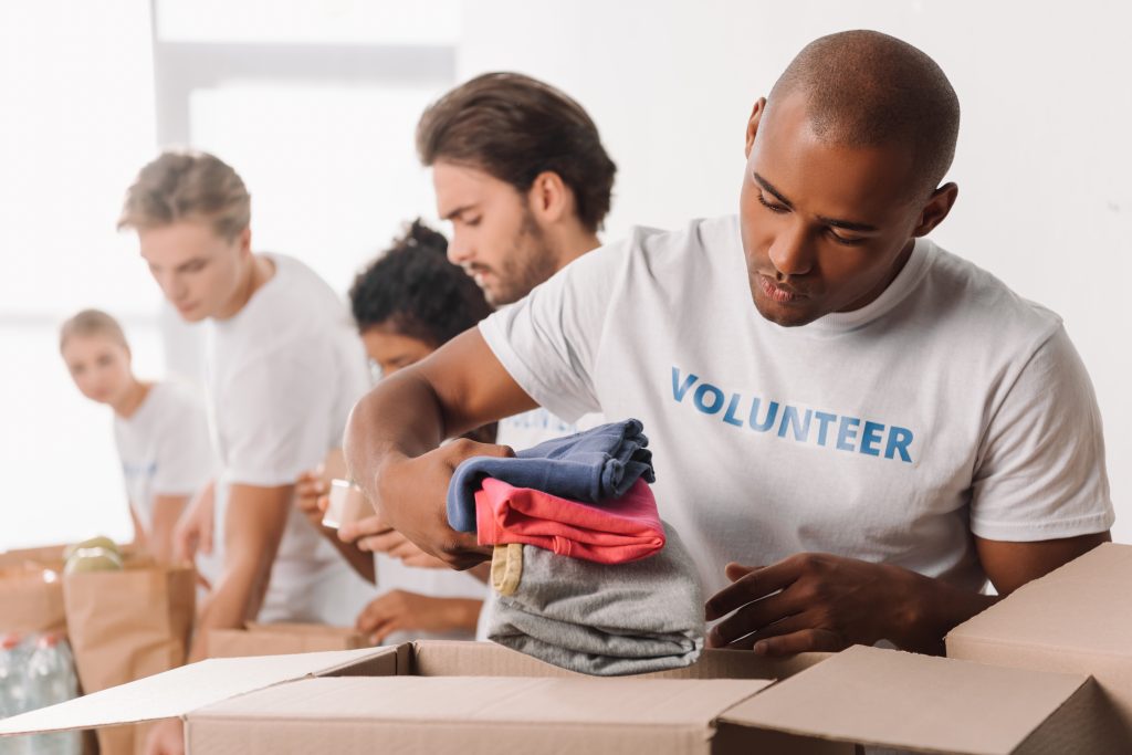 african american volunteer putting clothes in box for charity with blurred colleagues