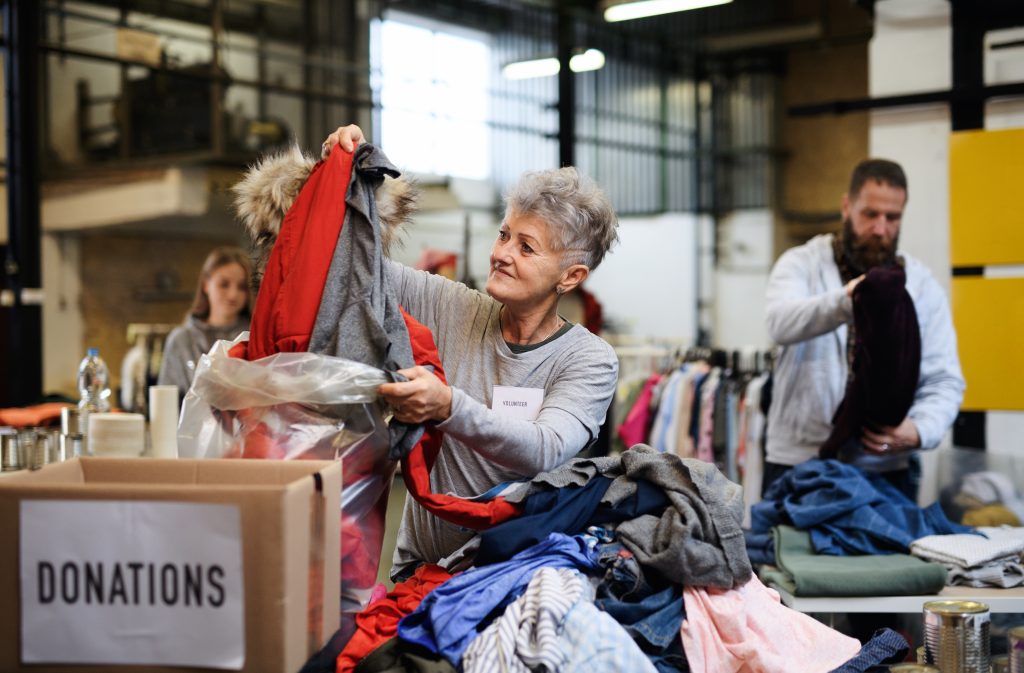Portrait of volunteers sorting out donated clothes in community charity donation center, coronavirus concept